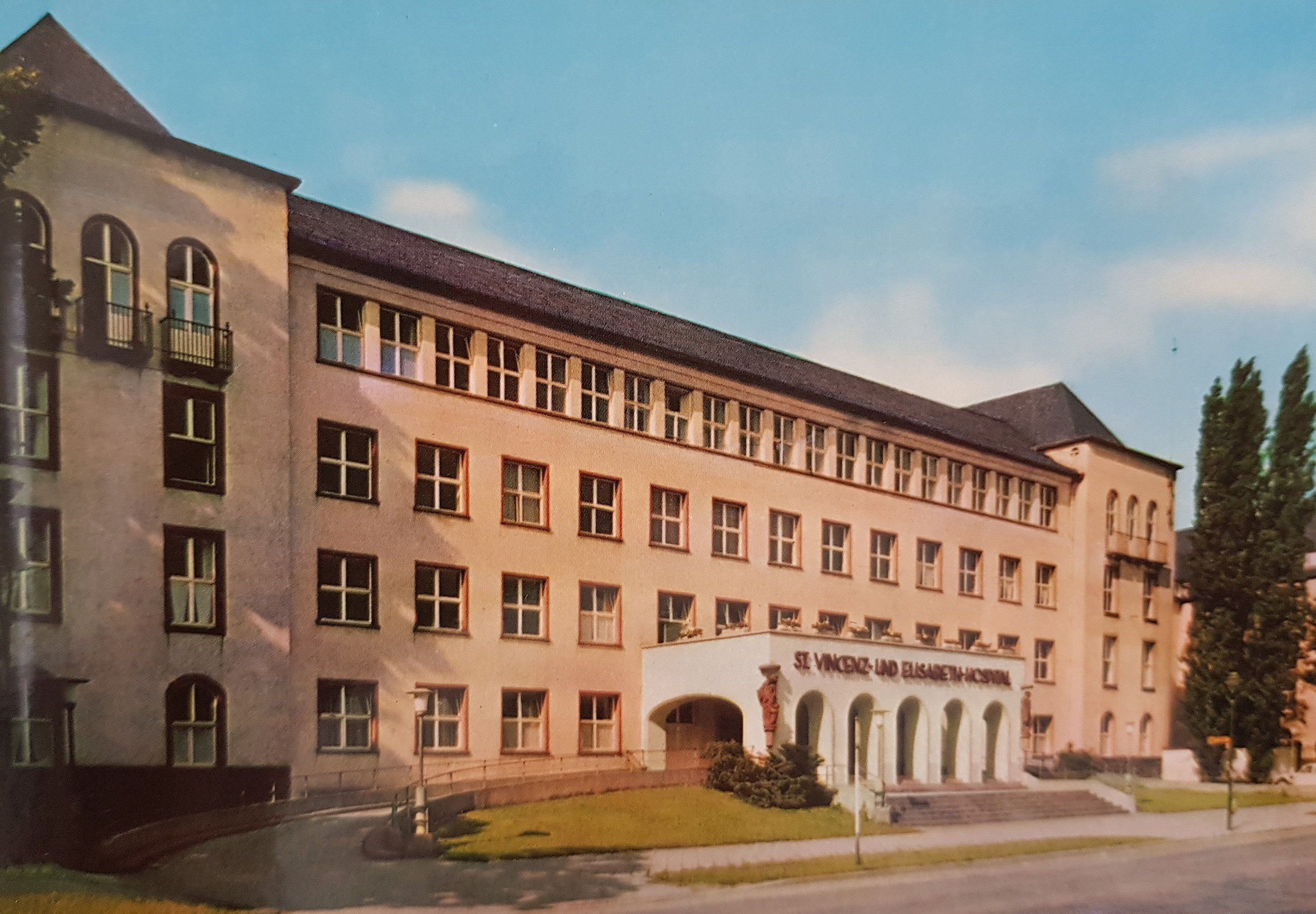 Fassade eines mehrstöckigen Gebäudes mit einem Eingangsbereich, der von Bögen umrahmt ist. Über dem Eingang steht 'St. Vinzenz und Elisabeth-Hospital'.