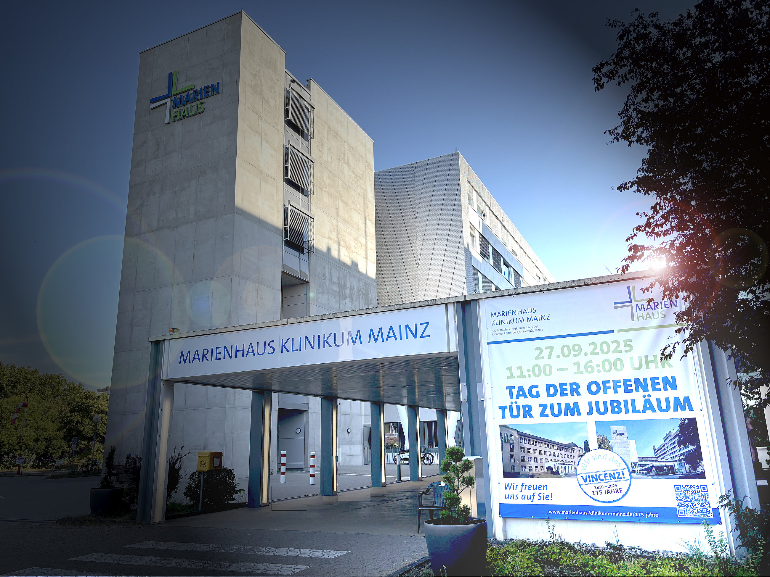 Das Marienhaus Klinikum Mainz, ein modernes Gebäude mit grauer Fassade und großen Fenstern. Vor dem Eingang hängt ein Banner mit dem Text 'TAG DER OFFENEN TÜR ZUM JUBILÄUM' und dem Datum '27.09.2025 11:00-16:00 UHR'.